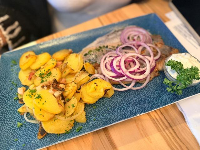 Gebratener Fisch mit Bratkartoffeln, roten Zwiebelringen und Kräuterquark auf einer blauen Platte