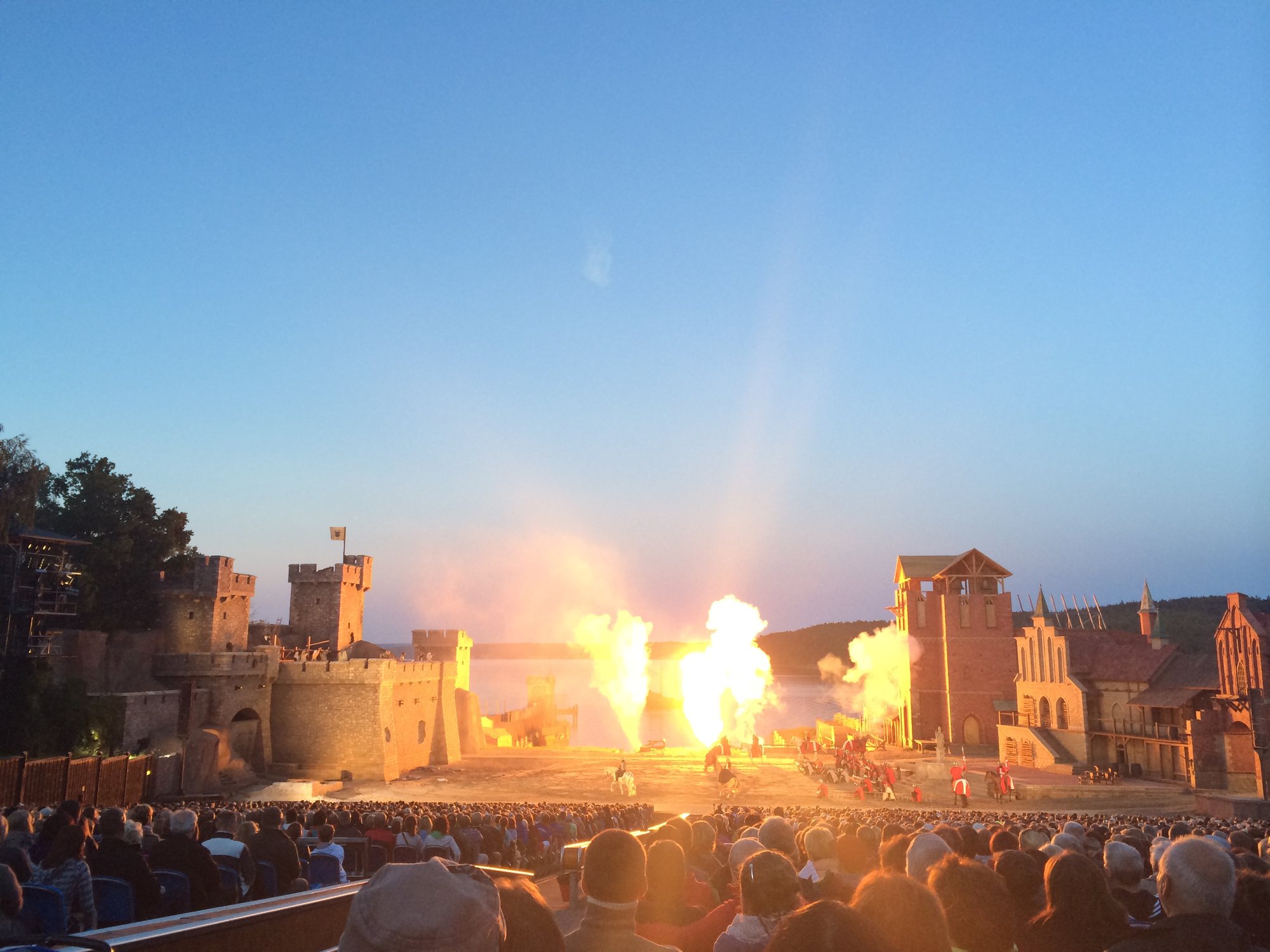 Störtebeker-Festspiele in Ralswiek am Abend: Feuerfontänen vor Burgkulisse und Bodden, davor voll besetzte Zuschauerränge