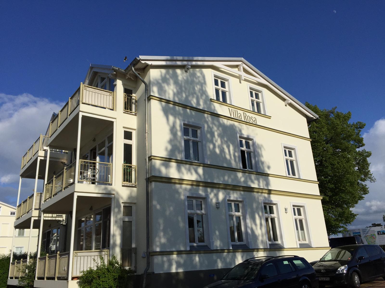 Die Villa Rosa in Glowe von außen: weißes Haus mit Balkonen und dem Schriftzug Villa Rosa unter blauem Himmel