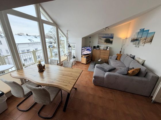 Wohn- und Essbereich: Holztisch vor der großen Fensterfront zum Balkon, rechts das graue Ecksofa