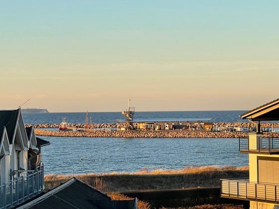 Blick auf Hafen und Ostsee im Abendlicht, vorn Hausdächer und Dünengras