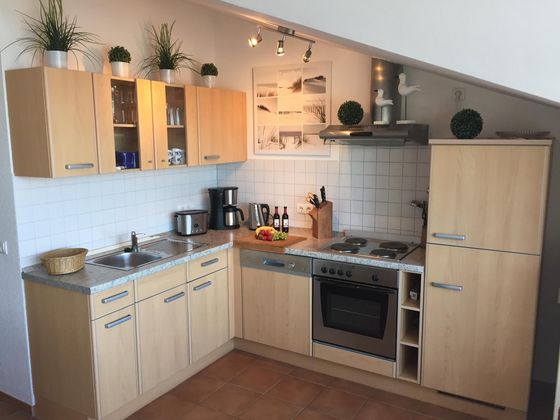 Einbauküche mit hellen Holzfronten unter der Dachschräge: Spüle, Toaster, Kaffeemaschine und Wasserkocher, Herd mit vier Kochplatten, Backofen und Geschirrspüler