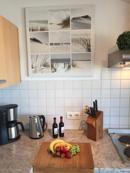 Arbeitsplatte mit Kaffeemaschine, Wasserkocher, Messerblock und Obst auf dem Schneidebrett, darüber ein Wandbild mit Dünenmotiven